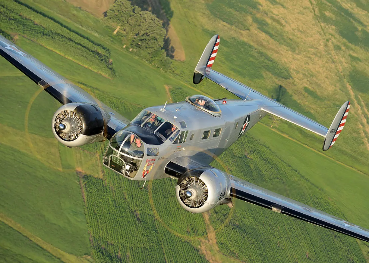 A vintage twin-engine airplane flying over green fields.