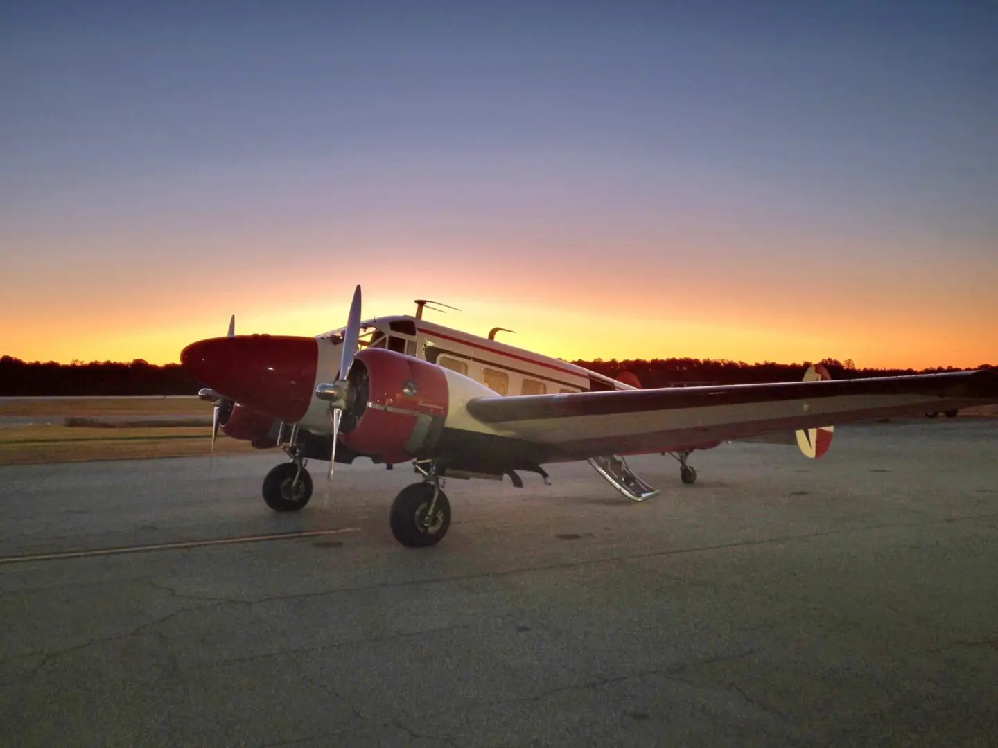 A vintage red and white airplane parked on a runway at sunset.