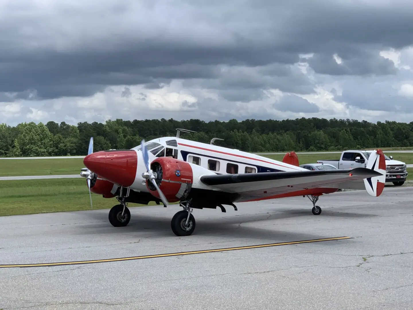 Vintage red, white, and black twin-engine airplane on runway under cloudy sky.