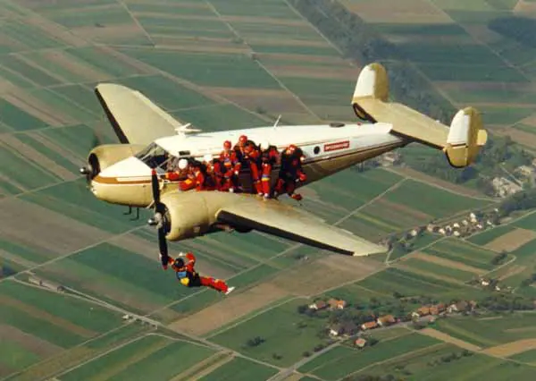 Skydivers jump from a vintage airplane over farmland.