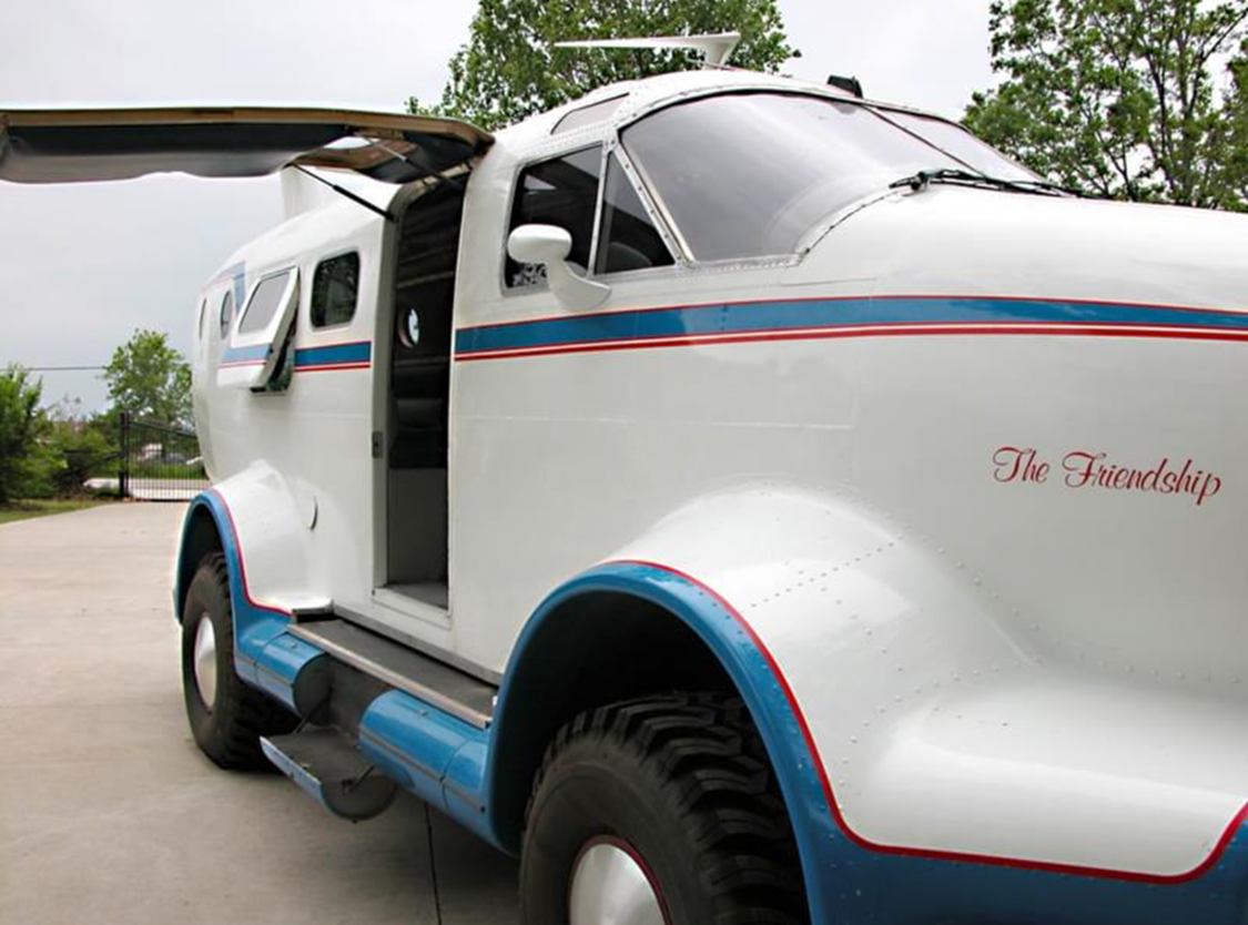 Vintage white delivery truck with blue and red stripes and open side door.