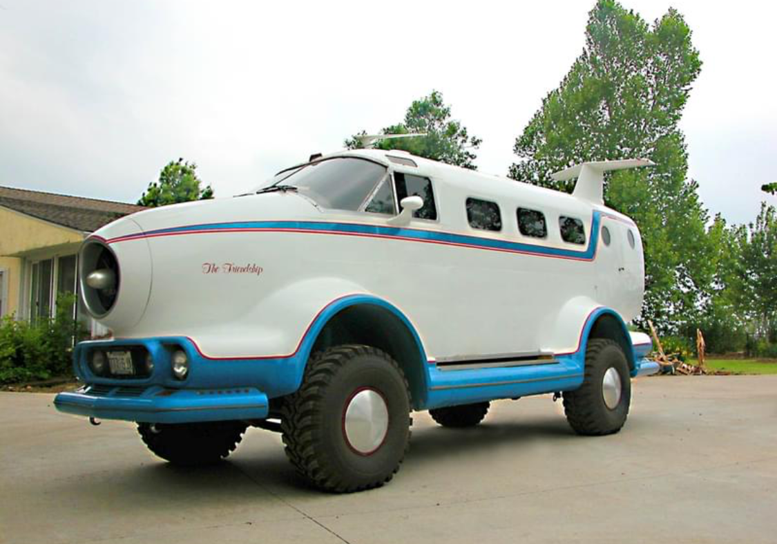A vintage white van with blue accents and large off-road tires.
