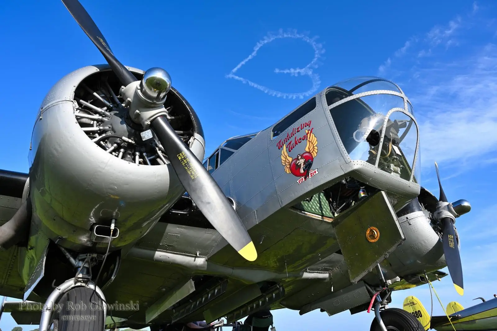 Vintage bomber airplane on display with skywriting in the background.