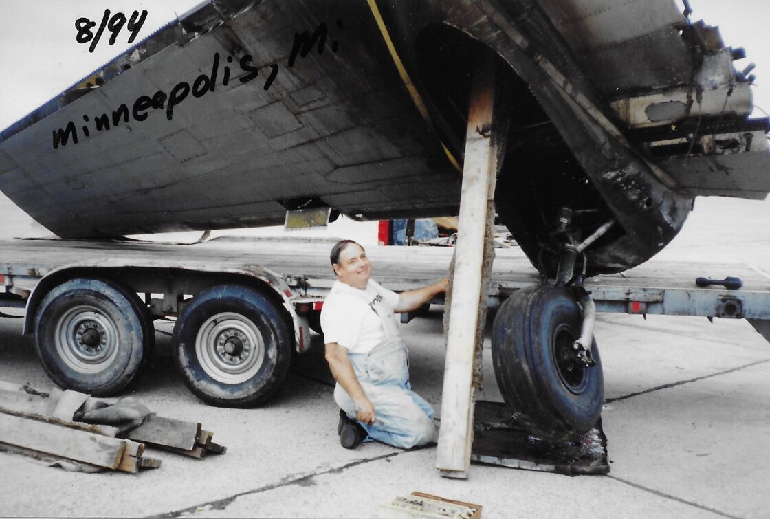 Man working on a large vehicle or aircraft undercarriage outdoors.