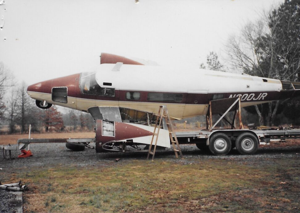 A trailer carrying a large airplane fuselage section in an outdoor area.