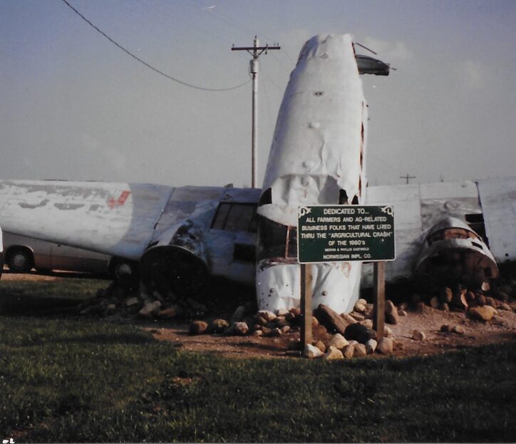 Damaged airplane nose lying on the ground near a sign.